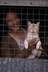 Woman carrying a cat behind a wire netting Burma