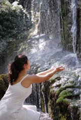 Young woman touching water at the foot of a waterfall Spain