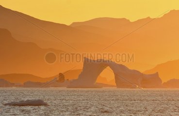 Denmark. Greenland. West coast. Sunset on an arch shaped iceberg in the straight of Vaigat  near the village of Saqqaq.