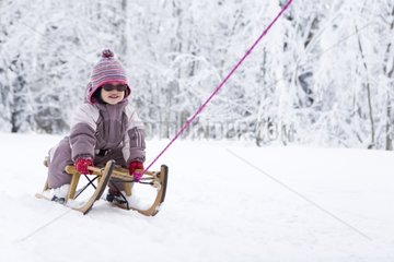 Little girl on a wooden sledge on a snowy runway