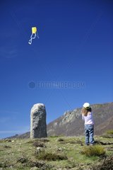 Girl playing kite in front of a Menhir Cevennes France