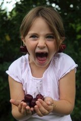Grimacing girl holding cherries in her hands - France