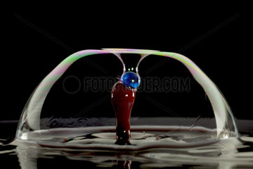 Drops of colored water and soap bubble on black background