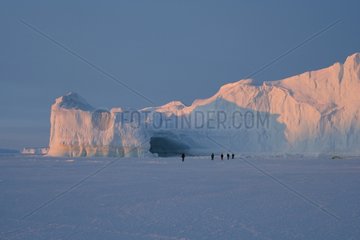 Hikers in front of an iceberg with a cave Adelie Land