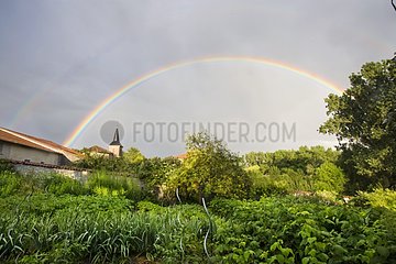 Rainbow above the steeple of a village and a garden