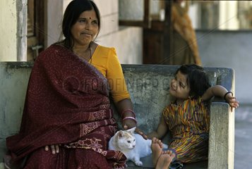 Cat lying down near a child and his mother on a bench India