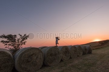 Girl jumping on rolls of straw at sunset