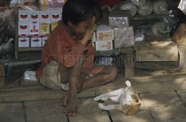 Kampuchean child playing with a cat lengthened on the ground