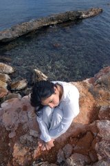 Femme pensive assisse sur des rochers côtiers