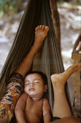 Child sleeping in a hammock between the legs of his mother