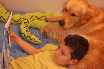 Enfant et golden retriver lisant sur un lit