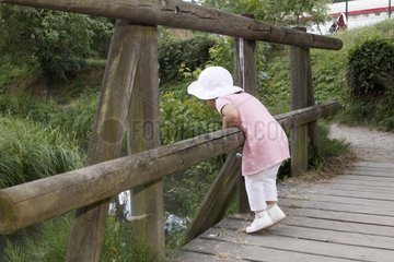 Girl looking at the fish from the top of a wooden bridge