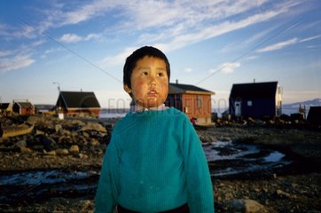 Jeune Inuit devant les maisons de son village