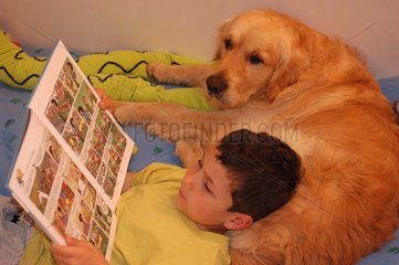 Enfant et golden retriever lisant sur un lit