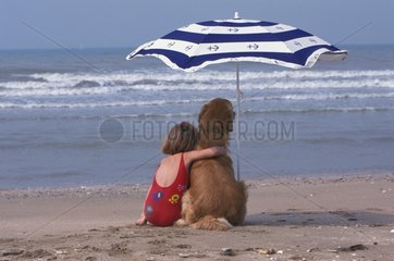 Fillette et son chien regardant la mer sous un parasol
