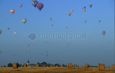 Hot air-balloon multitude flying over a field of roundballers
