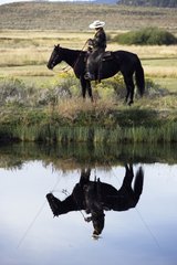 Cow-boy with horse and his reflection in water Oregon the USA