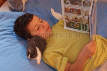 Enfant lisant dans son lit avec son lapin gris