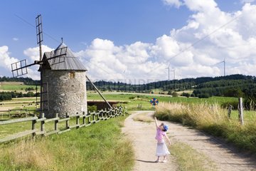 Little girl playing wind with a reel near a mill France