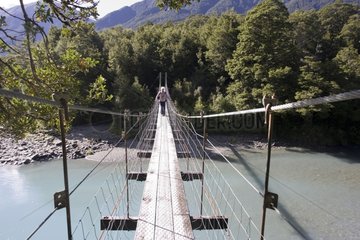 Tourist crossing wire suspension bridge over Haast River