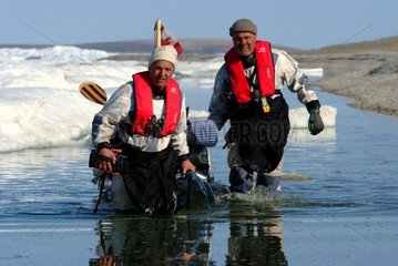 Men walk towing their kayak on the shore Arctic