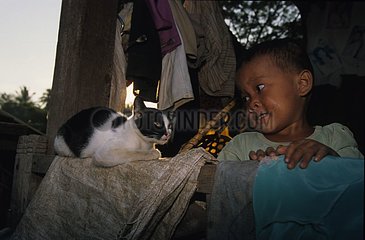 Kampuchean Kind schaut eine Katze an  die auf einem Strahl sitzt