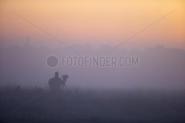 Photographer standing in the mist at sunrise in winter - GB