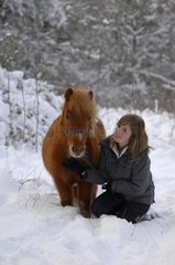 Young woman and chestnut Shetland Pony in snow - France