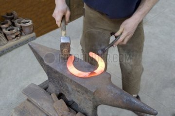 Blacksmith hammering a hot horseshoe France