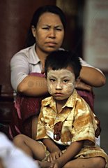 Boy with thanakha on face ahead of his mother Myanmar