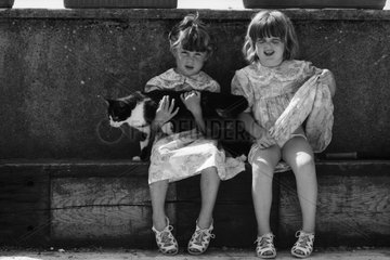 Young girls holding a cat on a bench