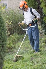 Man cutting grass with a weed-whacker in a garden in autumn