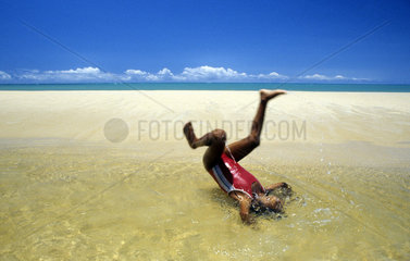 Arraial DAjuda  Bahia - Brazil. Black child plays in a pond formed by river water in the sands of a tropical beach. Somersault  handspring  black girl upside down.