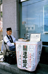 Kokura: Man with street stand practizing handreading and iridology.