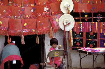 Mexico  Chiapas; small child selling traditional fabrics  all coloured red and hats
