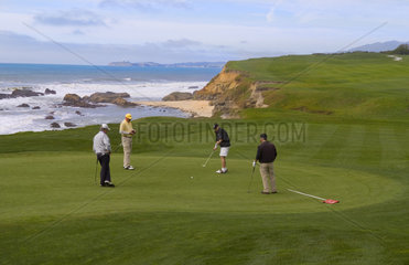 Men friends golfing at 18th green of the famous Old Course at Half Moon Bay California on ocean at Ritz Hotel