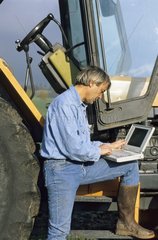 Bauer benutzt einen Laptop in der Nähe seines Traktors Frankreich