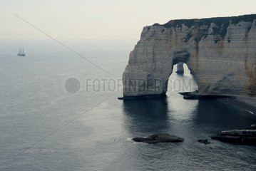 Arch of the cliffs of Etretat and sailboat in broad