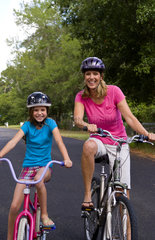 White mother and daughter having fun together outdoors with bikes and helmets for safety