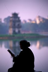 Old woman reading near water Hanoi Vietnam