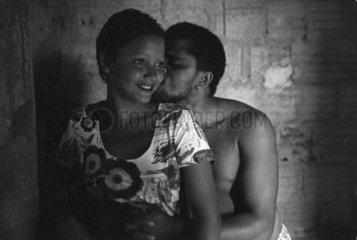 Adolescent black couple in love. Afro-descendent teenager kisses his beautiful girlfriend. Poor house  low income people. Happiness  tenderness.