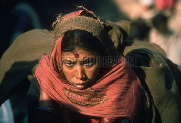 NEPAL : Kathmandu Valley. Peasant woman wiith a heavy load on the way to the market in Kathmandu. Early on a winter morning.