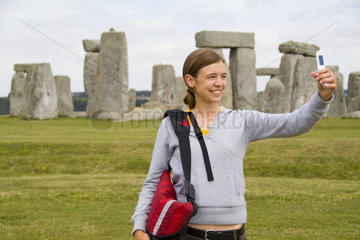 College age woman taking cell phone photo in front of the world famous Stonehenge monument in England Great Britian