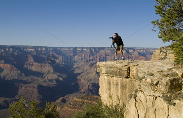 Adventurous photographer taking pictures perched high on cliff at beautiful early morning light at the South Rim of the famous Grand Canyon fron above in Arizona USA