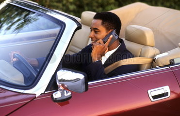 Successful black african american business man on cell phone while traveling in luxury convertible