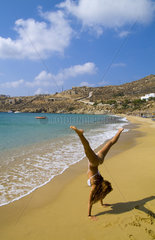 Beautiful island of Mykonos Greece with private beach called Super Paradise Beach and young shapely woman doing cartwheel exercise