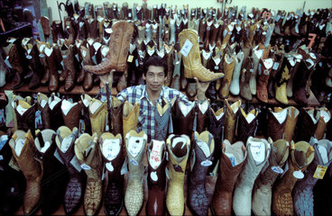 Mexico  Mexico City; a salesman in a shoeshop holding up two leather boots  standing in between neat rows of many cowboy boots