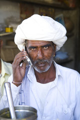 Traditional Hindu vendor man with white turban portrait using modern technology cell phone in Jaipur Rajasthan India