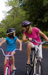 White mother and daughter having fun together outdoors with bikes and helmets for safety