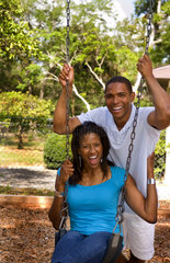 Black African American couple dating and playing on swing at playground